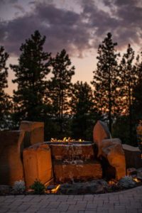Lake Fernan Residence - Passive House Institute Certified Fire pit with waterfall at sunset in forest setting.