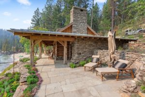 Rustic lakeside cabin with stone patio and chairs.