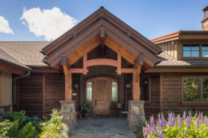 Rustic wooden house entrance with stone pillars.