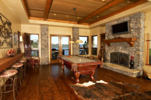 Rustic game room with pool table and stone fireplace.