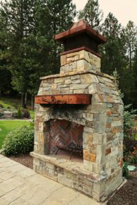 Stone outdoor fireplace with lush greenery.