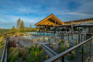 Modern hillside lodge with glass railings, outdoor seating, and stunning mountain views under a clear blue sky.