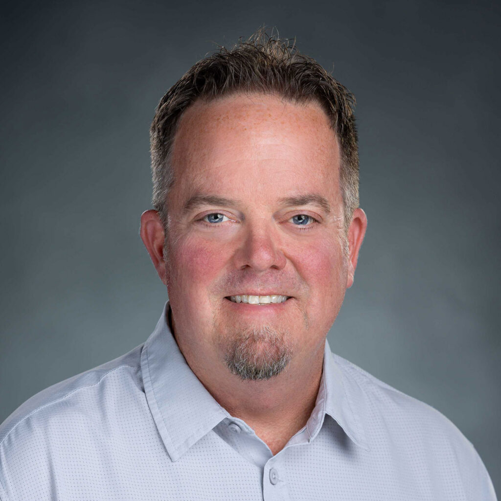 Smiling man in a light shirt against a gray background.
